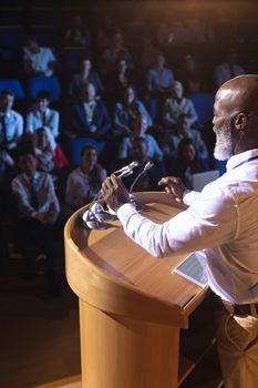 Side view of old African-American businessman standing and giving presentation in the auditorium 