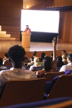 Front view of mixed race woman sitting in audience raising hand for asking question