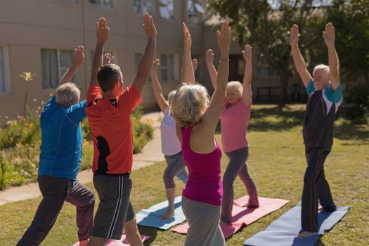 Rear view of trainer training senior people in performing exercise on yoga mat  at park