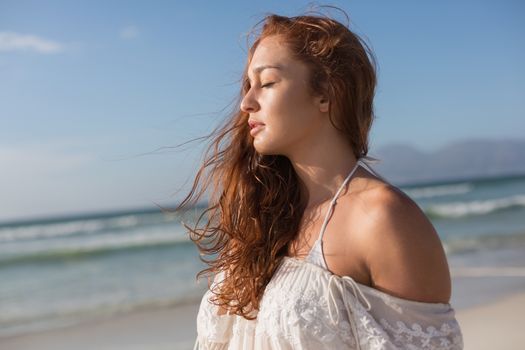 Side view of beautiful young Caucasian woman with eyes closed standing standing on the beach. She seems relaxed