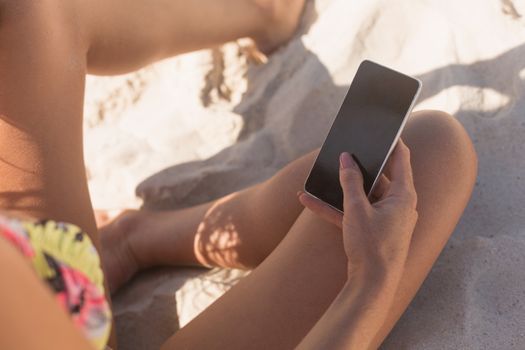 Close-up of young Caucaian woman in bikini her using mobile phone sitting at beach