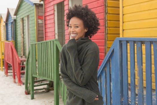 Front view of pretty happy young African American woman standing at beach hut. She is smiling