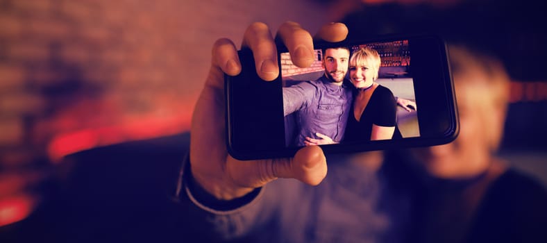 Smiling couple taking selfie on mobile phone in bar