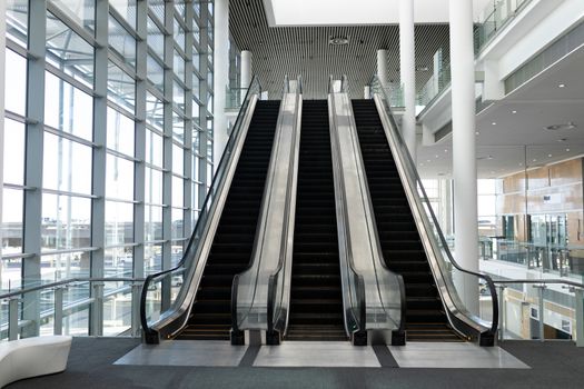 Front view of three modern escalators in a office lobby against inside buildings in background