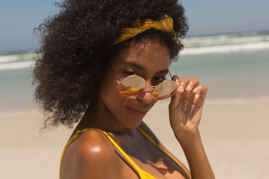 Portrait of young African American woman in bikini looking over sunglasses on the beach