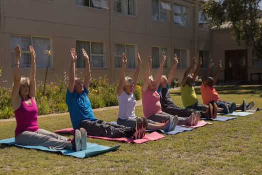 Side view of group of active senior people exercising gym aligned on yoga mat  in the park