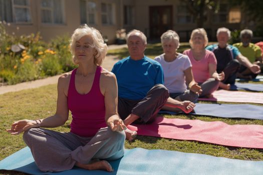 Front view of group of active senior people performing yoga in the park. They are sitting on yoga mat