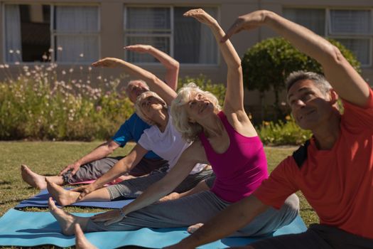 Side view of trainer training senior people in performing exercise on yoga mat at park