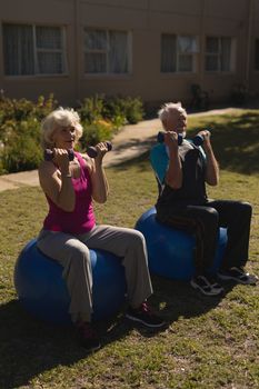 Frontv iew of active senior couple exercising with dumbbells on exercce ball in the park