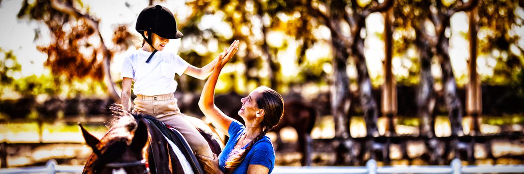 Side view of woman giving high five to girl sitting on horse in paddock