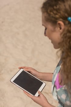 Side view of gorgeous young Caucasian woman using digital tablet standing on the beach on a sunny day. She is smiling