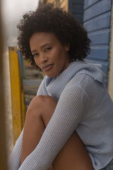 Portrait of happy young African American woman standing at beach hut. She is smiling and looking at camera