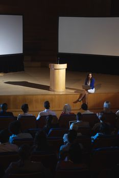 High view of beautiful businesswoman sitting at the side of the stage and having laptop in her hand in front of audience