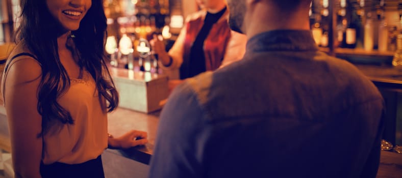 Smiling friends interacting at counter in bar