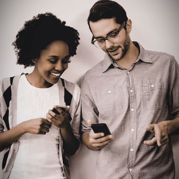 Man and woman standing against white wall and using mobile phone in office