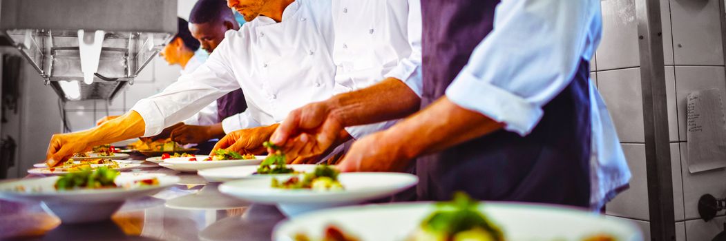 Team of chefs garnishing meal on counter in commercial kitchen