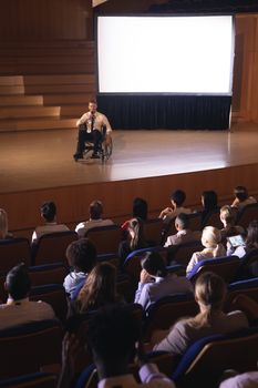 High view of Caucasian businessman sitting on a wheelchair and giving presentation to the audience in the auditorium