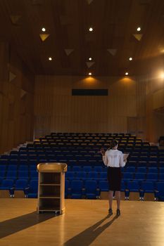 Rear view of blonde Caucasian businesswoman practicing and learning script while standing in the auditorium