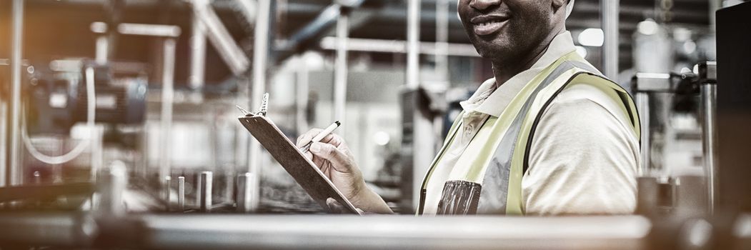 Portrait of smiling factory worker writing on clipboard in factory