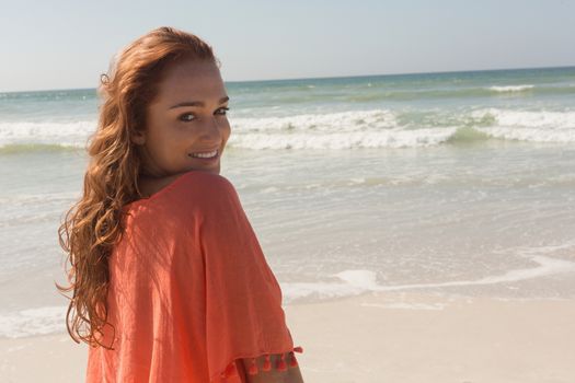 Side view of happy beautiful young Caucasian woman looking at camera on the beach.She is smiling