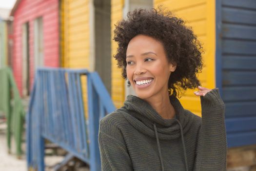 Front view of pretty happy young African American woman standing at beach hut. She is smiling