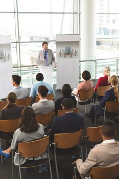 High angle view of Caucasian male speaker with laptop having a presentation in front of business people sitting at business seminar in office building