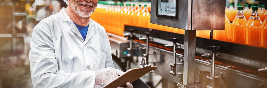 Portrait of smiling factory engineer maintaining record on clipboard in drinks production plant