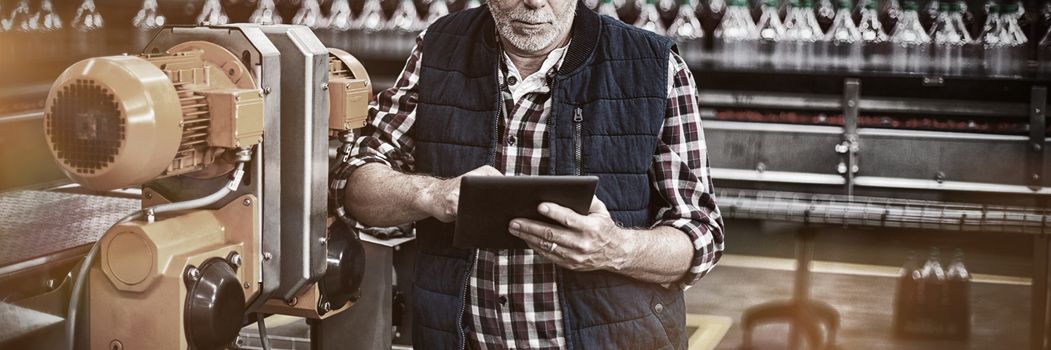 Factory worker using digital tablet next to production line in drinks production plant