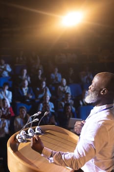 High angle view of old African-American businessman standing near podium and giving speech to the audience in the auditorium