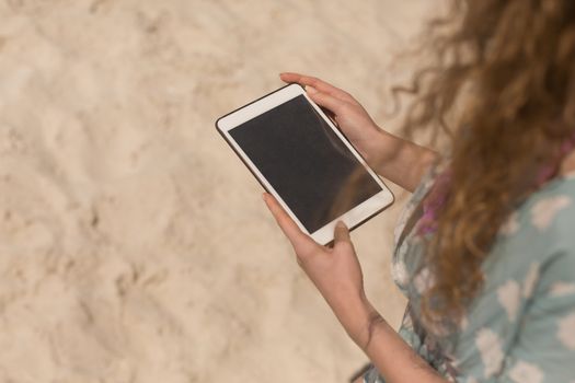Midsection of young Caucasian woman using digital table on beach. It is sunny day