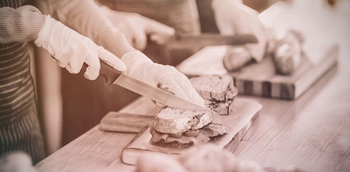 Mid-section of waiter chopping bread roll and sandwich on chopping board in cafÃ©