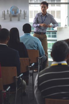 Front view of young well dressed Asian businessman speaking to business professionals sitting at business seminar in office building