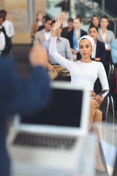 Front view of businesswoman raising hand in a business seminar in office