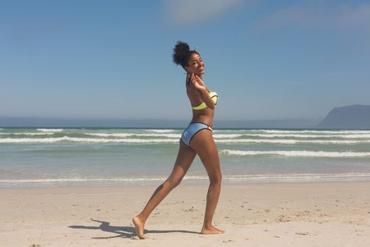 Portrait of pretty happy young African American woman in green bikini playing on the beach. She is smiling and looking at camera