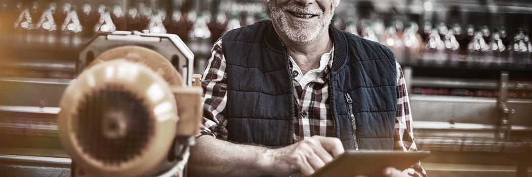 Portrait of smiling factory worker standing with a digital tablet in drinks production plant