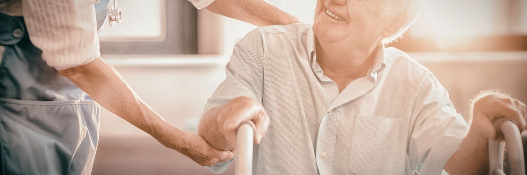 Female doctor helping senior man to walk with walker at home