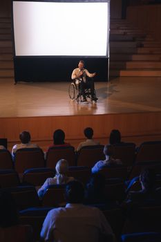 Front view of Caucasian businessman sitting on a wheelchair and giving presentation to the audience in the auditorium