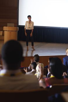 Front view of beautiful Asian businesswoman standing and giving presentation in front of the audience in auditorium 