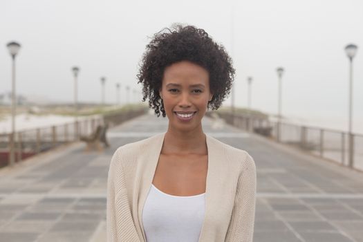 Portrait of happy young African American woman looking at camera on promenade. She is smiling