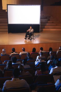 High view of Caucasian businessman sitting on a wheelchair and giving presentation to the audience in the auditorium