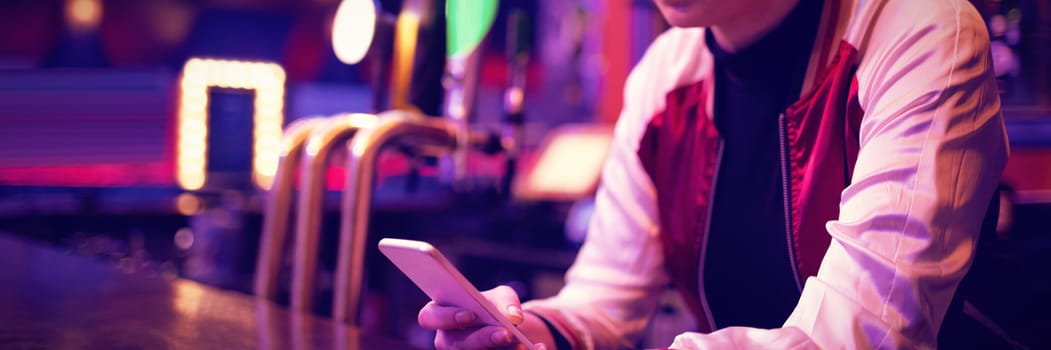 Female bartender using mobile phone at counter in bar