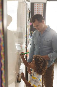 Side view of a Caucasian teacher teatching something to a metis school boy on a whiteboard