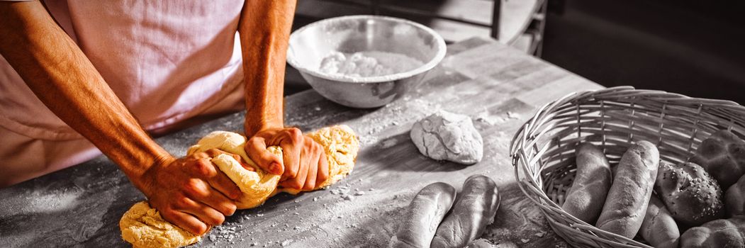 Mid-section of baker kneading a dough in bakery shop