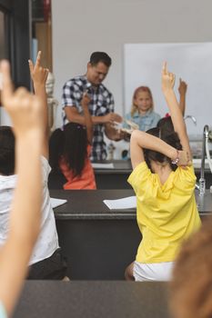 Rear view of school kids raising hand at school while teacher and a volunteer schoolgirl exposing an animal skull