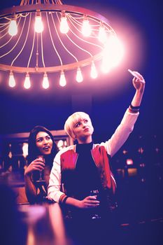 Smiling friends taking a selfie while having wine in bar