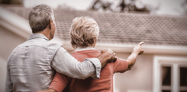 Rear view of senior couple looking at house while standing in yard 