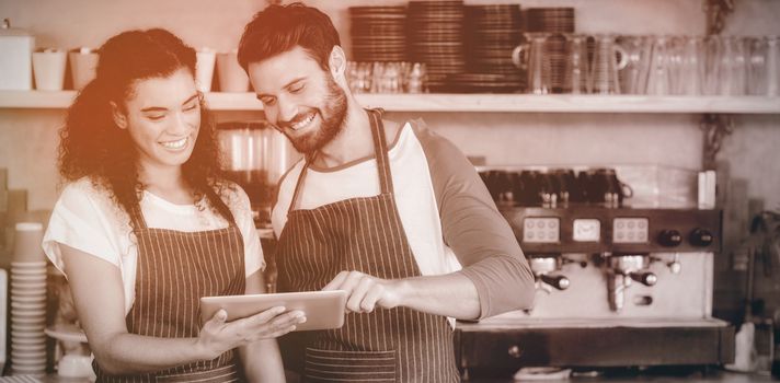 Smiling waiter and waitress using digital tablet at counter in cafe