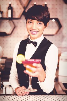 Portrait of smiling bartender holding glass of cocktail in counter at bar