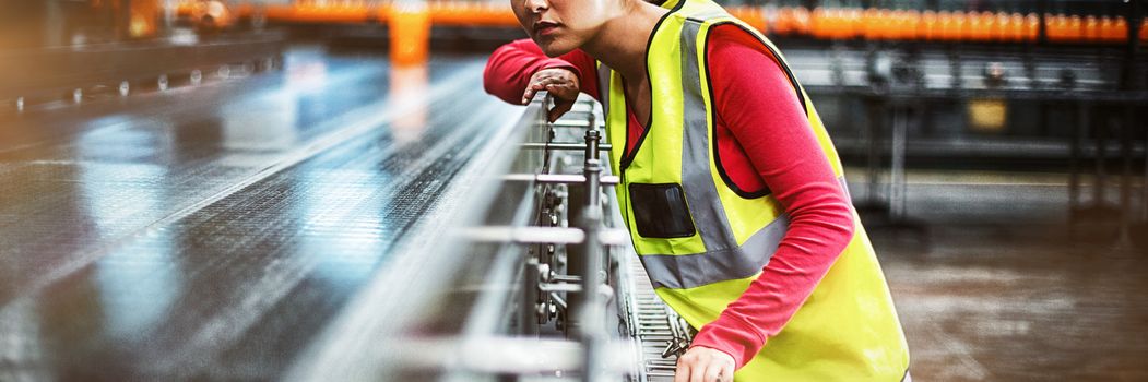 Female factory worker checking conveyor belt at drinks production factory