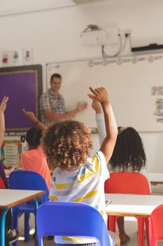 Rear view of school kids raising hand to answer at a question while the teacher speaking at whiteboard